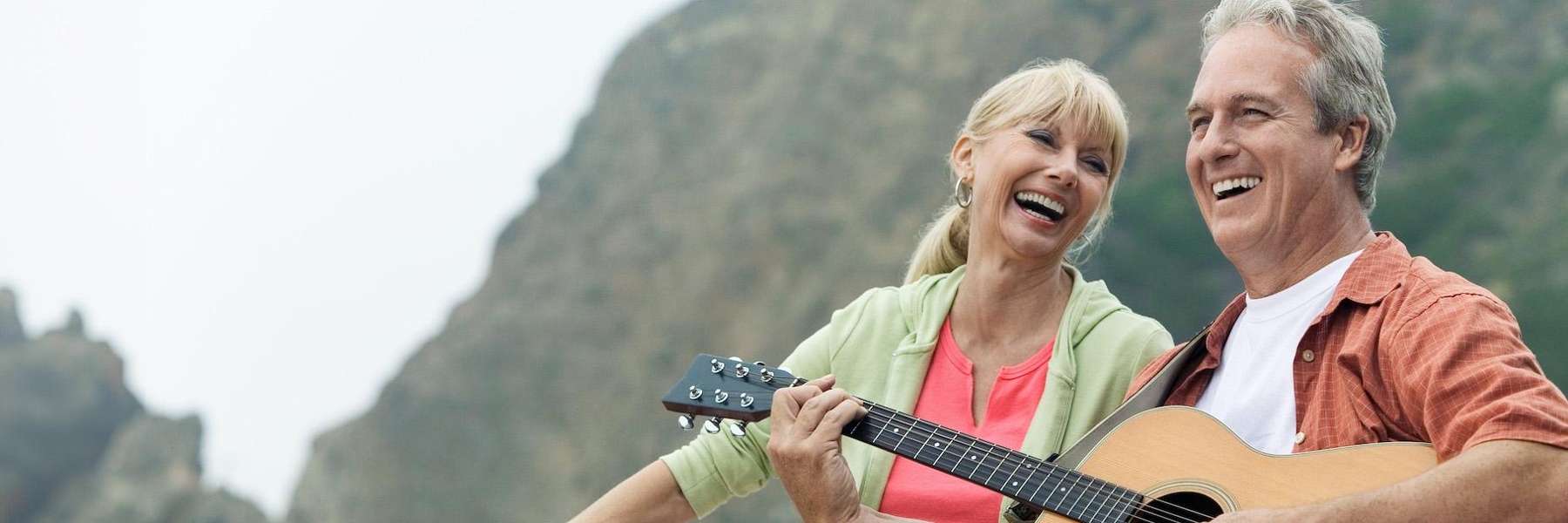 man playing acoustic guitar while a woman listens sitting on the beach