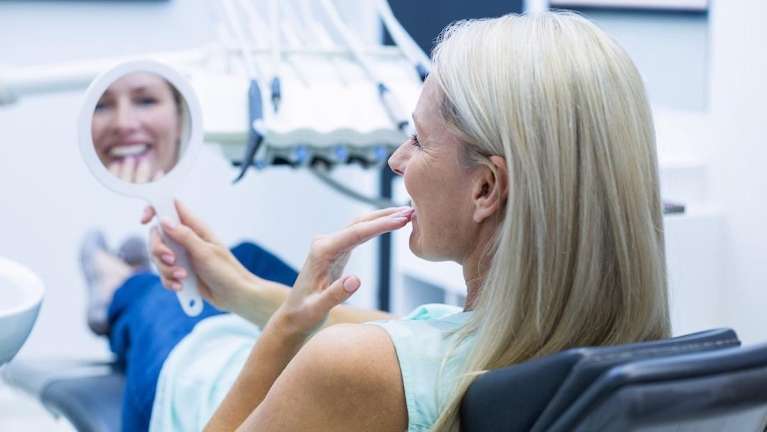 woman smiling into a dental mirror after getting a crown