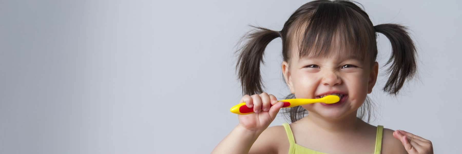 young girl with pigtails smiling while brushing her teeth