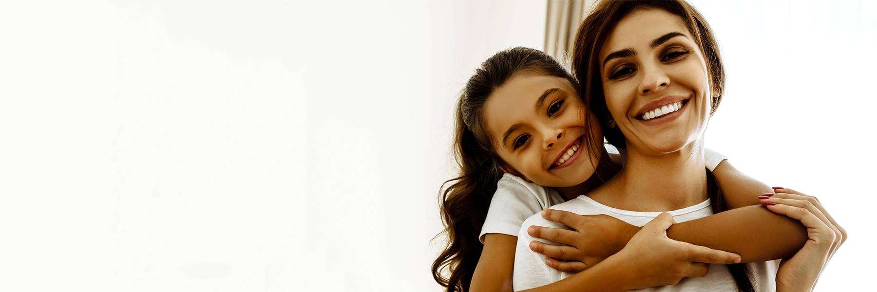 young girl smiling her and hugging her mom's shoulders